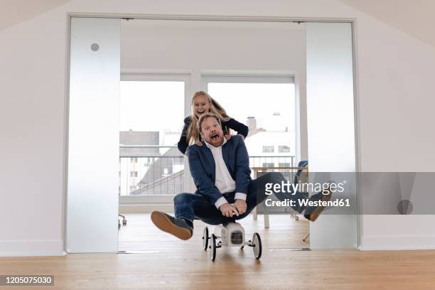 playful businesswoman pushing businessman on toy car in office - toy car foto e immagini stock