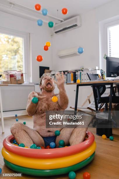 crazy businessman sitting in wading pool in office playing with balls - hairy chest man stock pictures, royalty-free photos & images