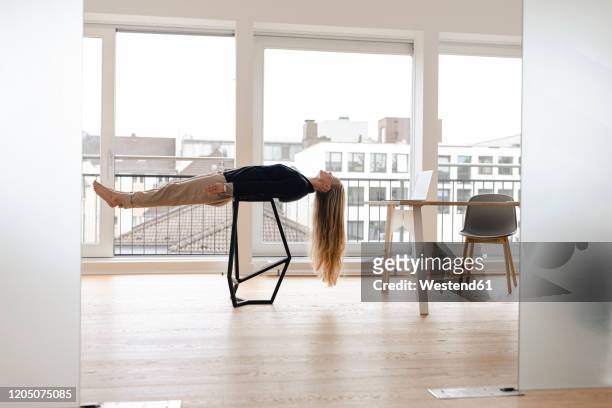 young businesswoman practicing yoga in office lying on a stool - hovering fotografías e imágenes de stock