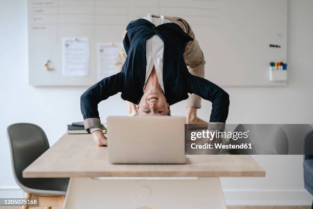 young businesswoman practicing yoga on desk in office - büro sport stock-fotos und bilder