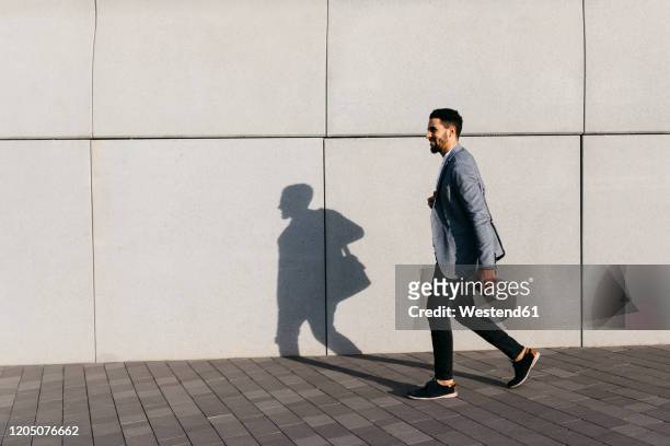 casual young businessman walking along the wall in the city - gehen stock-fotos und bilder