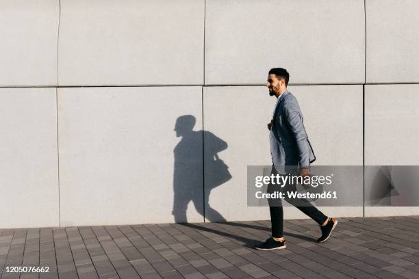 casual young businessman walking along the wall in the city - gray jacket imagens e fotografias de stock