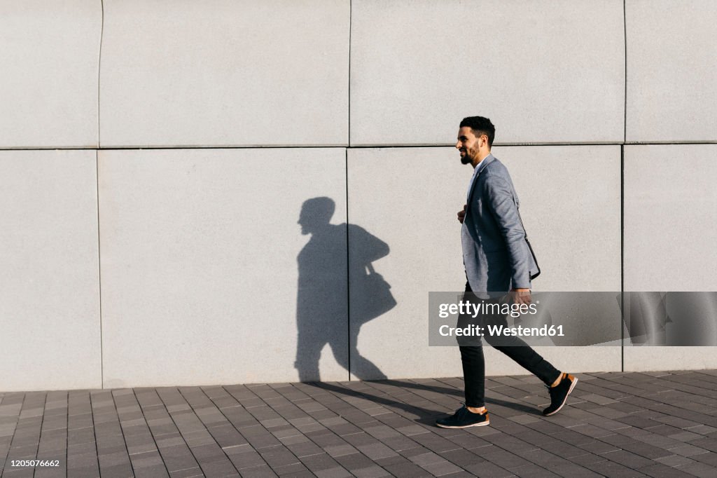 Casual young businessman walking along the wall in the city