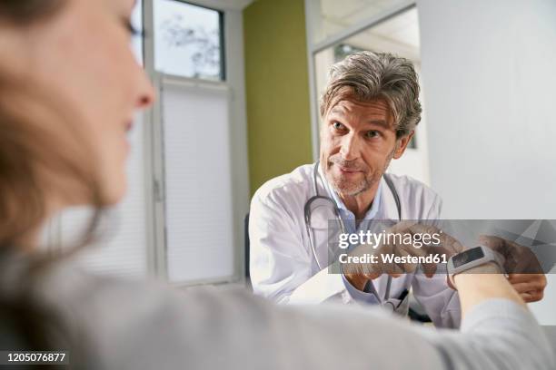 doctor checking smartwatch of female patient in his medical practice - wearable stock-fotos und bilder