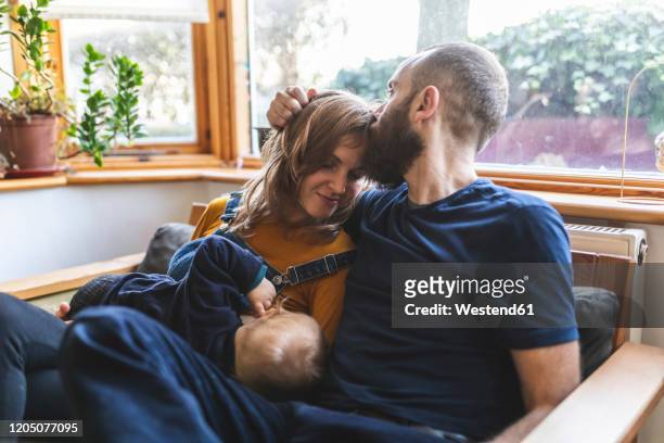 woman on the sofa breastfeeding her little son and sharing time with her husband - two parents stock-fotos und bilder