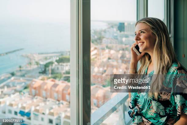 smiling woman on the phone at the window in coastal town - hawaiian shirt imagens e fotografias de stock