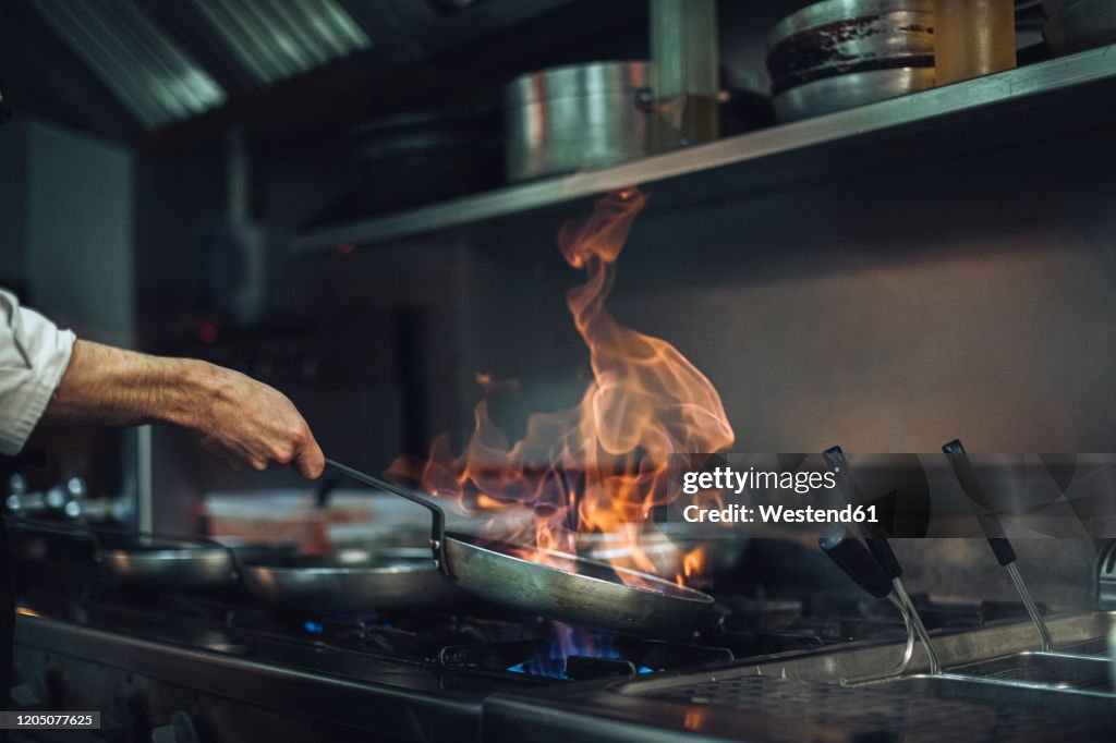 Chef preparing a flambe dish at gas stove in restaurant kitchen