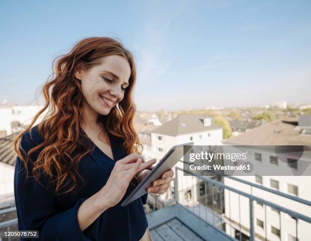 smiling redheaded woman using tablet on rooftop terrace - business woman blue stock pictures, royalty-free photos & images