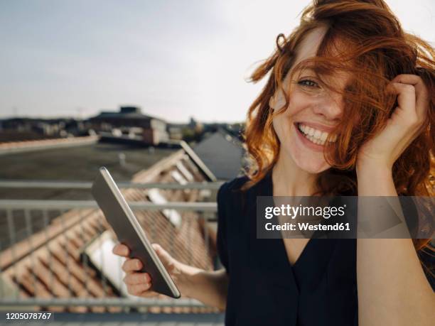 portrait of happy redheaded woman with tablet on rooftop terrace - tossing hair facing camera woman outdoors stock pictures, royalty-free photos & images