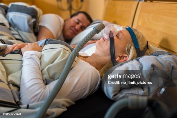 femme utilisant le masque de cpap en raison de l’apnea obstructif de sommeil, son mari est à côté - ventilator photos et images de collection
