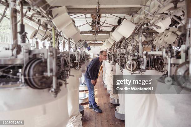 man working at a machine in a textile factory - fábrica textil fotografías e imágenes de stock