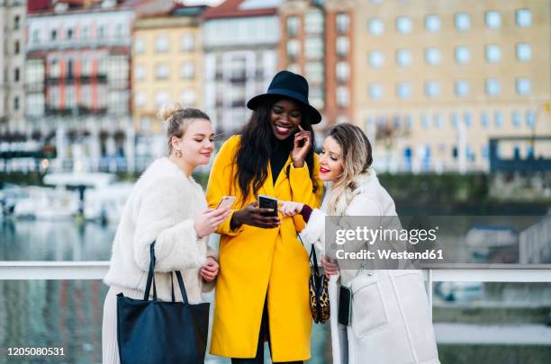 girlfriends using mobile phone at the marina in the city - yellow jacket stockfoto's en -beelden