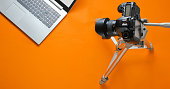 Online concept blogger, reviewer. Camera on tripod, laptop on orange background. Minimalism.