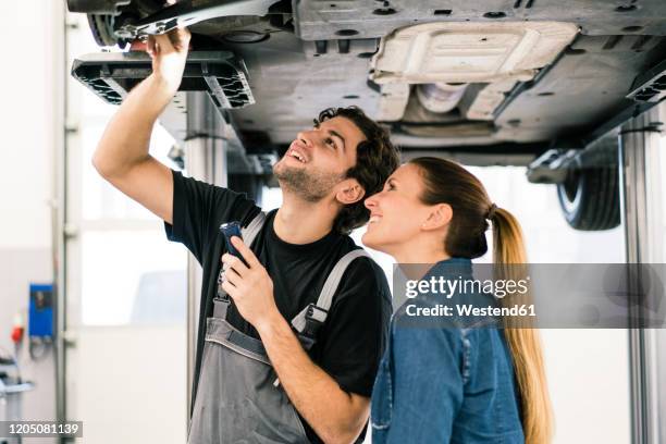 car mechanic talking to client in workshop - reparatiewerkplaats stockfoto's en -beelden