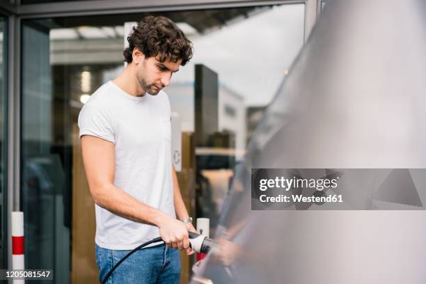 man charging an electric car at a station - elektroauto tanken stockfoto's en -beelden