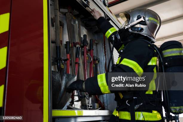 bombero cargado su equipo de oxigeno y mascara busca una herramienta en su camion para la emergencia. - motor de busca stock-fotos und bilder