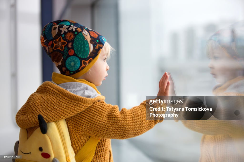 Blond toddler boy with family, traveling with airplane, running at the airport with suitcase