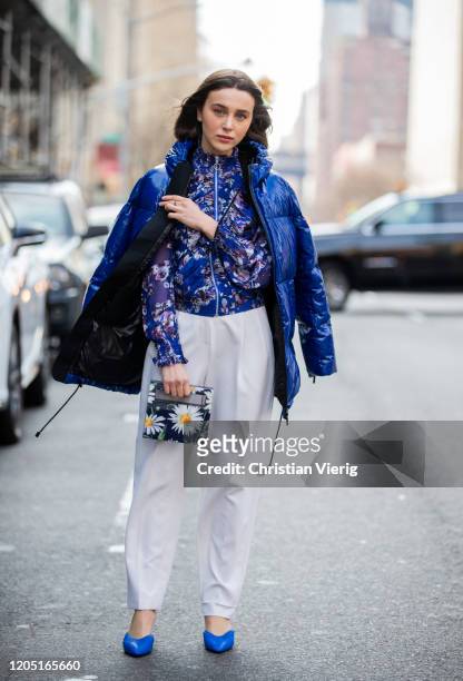 Mary Leest is seen wearing blue down feather jacket, bag with floral print, white pants, zipper jacket outside Tory Burch during New York Fashion...
