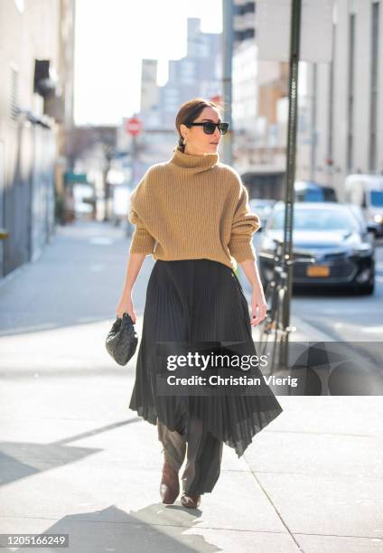 Geraldine Boublil is seen wearing brown turtleneck knit, black asymmetric pleated skirt worn over pants, black Bottega bag outside Tory Burch during...