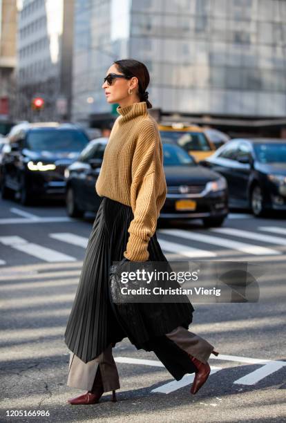 Geraldine Boublil is seen wearing brown turtleneck knit, black asymmetric pleated skirt worn over pants, black Bottega bag outside Tory Burch during...