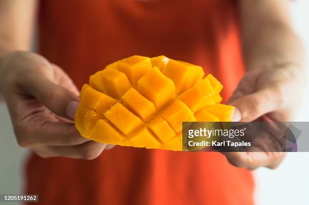a young woman is holding a freshly sliced ripe mango - mature adult foto e immagini stock
