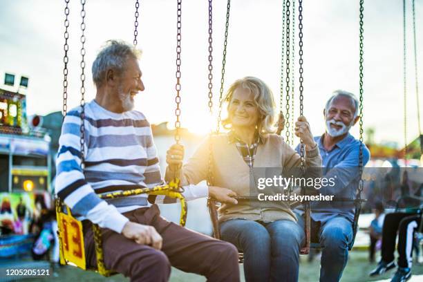 happy senior friends talking on chain swing ride. - carousel swings stock pictures, royalty-free photos & images