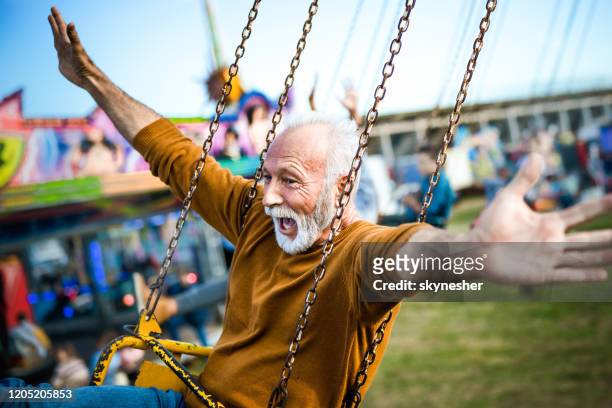 glücklicher reifer mann mit spaß auf einer kettenschaukel fahrt im vergnügungspark. - senior adult stock-fotos und bilder