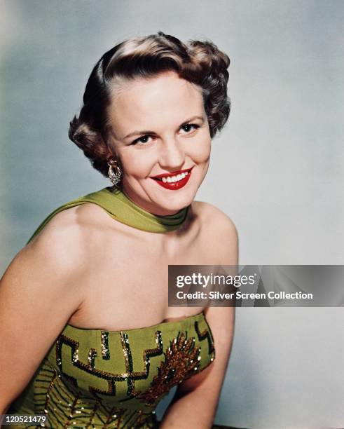 Peggy Lee , US singer, songwriter and actress, smiling, wearing a green strapless dress and a green scarf, in a studio portrait against a pale blue...