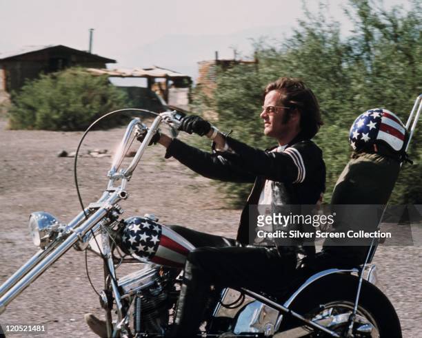 Peter Fonda, US actor, riding a chopper motorcycle, with a stars-and-stripes helmet on the backrest of his seat, in a publicity still issued for the...