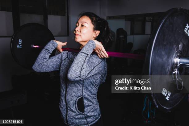 asian senior woman lifting weight in a gym - asian female bodybuilder stock-fotos und bilder