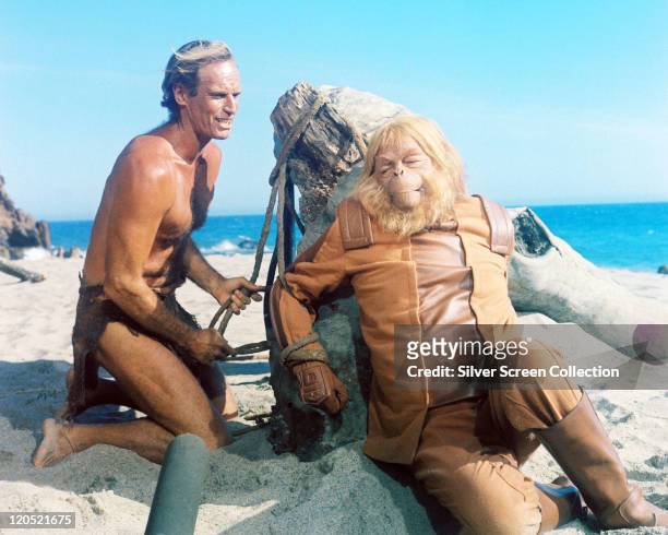 Charlton Heston , US actor, wearing a loin cloth as he ties Maurice Evans , British actor, in costume and wearing an ape mask in a publicity still...