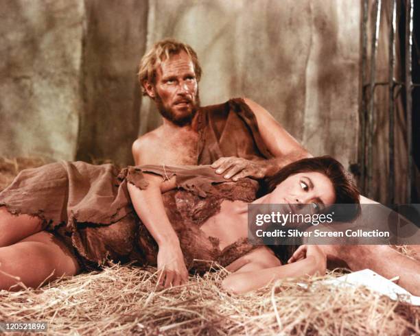 Charlton Heston , US actor, and Linda Harrison, US actress, both wearing animal hides, laying on straw in a publicity still issued for the film,...