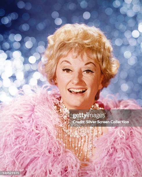 Phyllis Diller, US actress and comedian, wearing a pink feather boa, against a shimmering blue background, circa 1965.