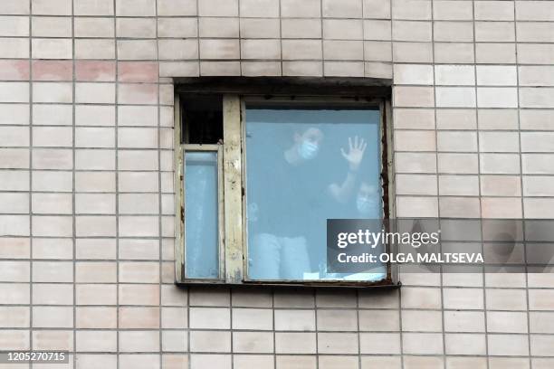 People wearing facemasks are seen in the window of a quarantined building housing the dormitory of the North-Western State Medical University named...