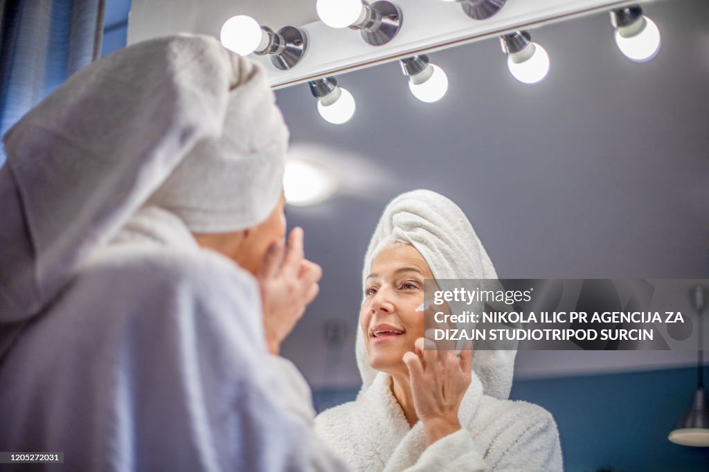 Mature woman applying face cream.