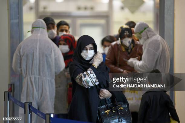 Medical staff in protective gears distribute information sheets to Iraqi passengers returning from Iran at Najaf International Airport on March 5,...
