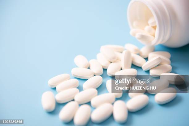 calcium pills pouring out of bottle on blue background - calcita fotografías e imágenes de stock