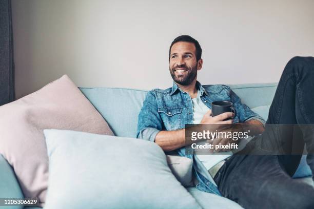 mann entspannt auf der couch - zurücklehnen stock-fotos und bilder