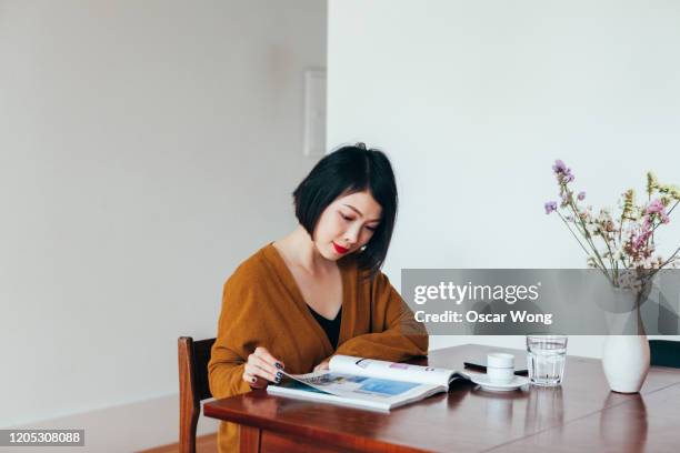 young woman reading magazine at dining table - magazine table ストックフォトと画像