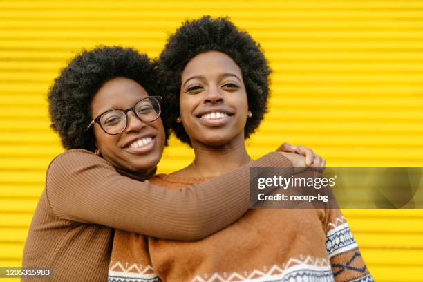 portret van gelukkige tweelingzusters voor gele achtergrond - adult twins stockfoto's en -beelden