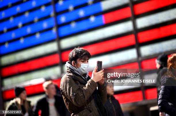 Man wears a mask as uses his cellphone at Times Square in front of an American flag on March 5, 2020 in New York City.