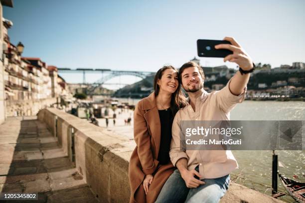 pareja joven tomando una foto selfie con un teléfono inteligente moderno - couple traveler fotografías e imágenes de stock