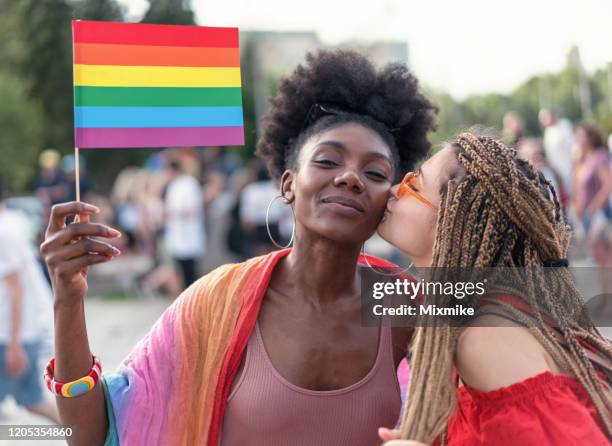 lovely female couple having fun at the lgbtqi parade - black lesbians kiss stock pictures, royalty-free photos & images