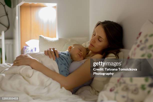 young beautiful mother sleeping her newborn baby boy at night dim light. mom breastfeeding infant - mother sleeping baby bildbanksfoton och bilder