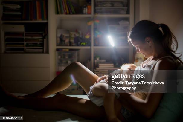 young beautiful mother breastfeeding her newborn baby boy at night dim light. mom breastfeeding infant - baby night stock-fotos und bilder