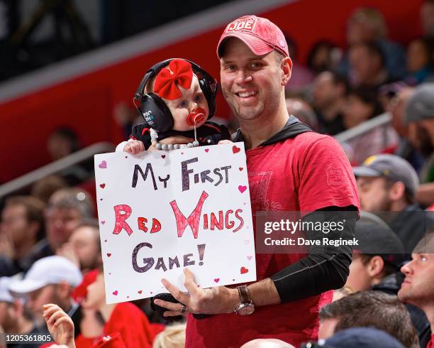 Dad holds his young daughter and their sign during an NHL game between the Detroit Red Wings and the Boston Bruins at Little Caesars Arena on...