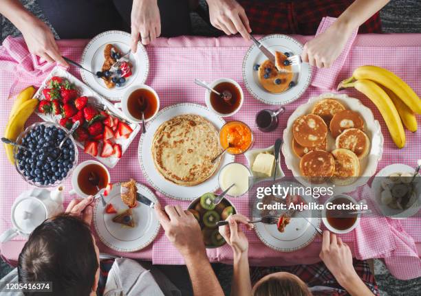 breakfast table. flat lay of eating peoples hands over breakfast table with crepes, pancakes, tea and berries. - frühstück von oben stock-fotos und bilder