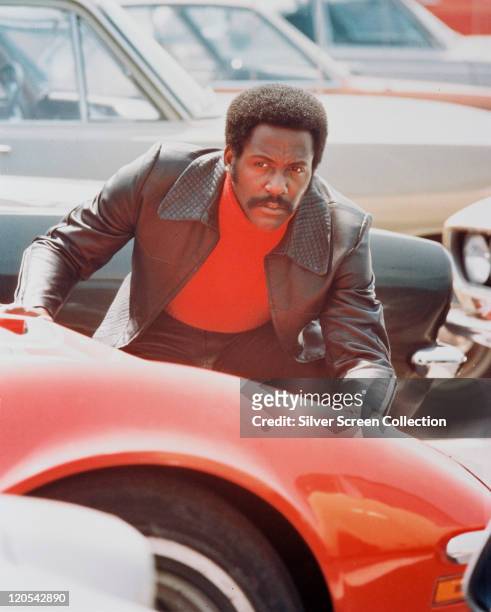 Richard Roundtree, US actor, crouching behind a red sports car in a publicity still issued for the film, 'Shaft', 1971. The blaxploitation film,...