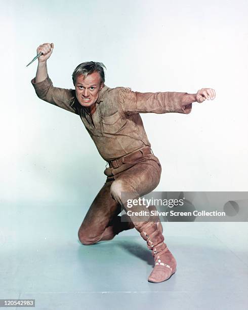 Richard Widmark , US actor, in costume, crouching and brandishing a knife, in a studio portrait, against a white background, issued as publicity for...