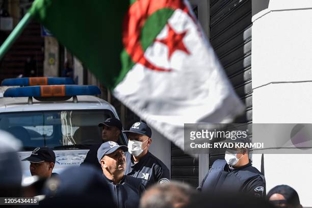 Algerian anti-riot police members wearing protective health masks stand as protesters march past them during a weekly anti-government demonstration...